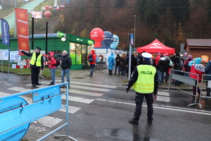 grafika-dzień, droga, policjanci na drodze i przejście dla pieszych, w tle skocznia i radiowozy oraz kibice