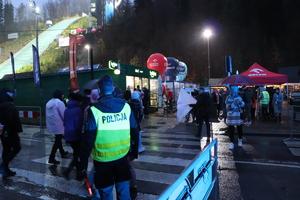grafika-noc, droga, policjanci na drodze i przejście dla pieszych, w tle skocznia i radiowozy oraz kibice