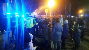 zdjęcie-policjanci rozdają odblaski pieszym na parkingu, noc, widoczne wozy policyjne i straży pożarnej z włączonymi niebieskimi sygnałami uprzywilejowania