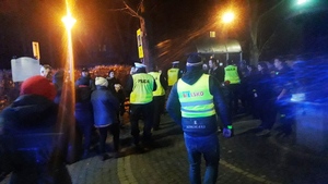 zdjęcie-policjanci rozdają odblaski pieszym na parkingu, noc, widoczne wozy policyjne i straży pożarnej z włączonymi niebieskimi sygnałami uprzywilejowania