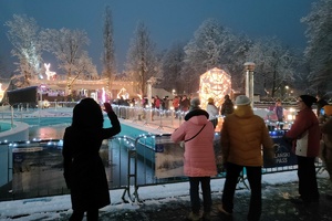 noc, zima, ludzie oglądają atrakcje świetlne widoczne na drugim planie