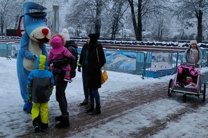 zdjęcie-policyjna maskotka pies Sznupek wręcza odblaski, zima, pochmurno,