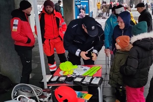 grafika- dzień, zima, pochmurno, policjant wręcza odblaski