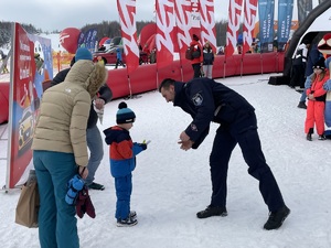 grafika-śnieg, zima, stok, dzieci i dorośli, policjanci rozmawiają z nimi i robią zdjęcia