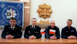 zdjęcie-pomieszczenie, sztuczne światło, przedstawiciele polskiej i czeskiej policji siedzą za stołem, na stole flagi polski i Czech