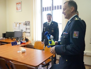 zdjęcie, pomieszczenie, jasno, komendant czeskiej policji się uśmiecha, trzyma w rękach otrzymany prezent, maskotkę Sznupka