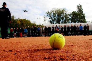 Zdjęcie - dzień, kort tenisowy, piłka do tenisa, w tle osoby ustawione w rzędzie