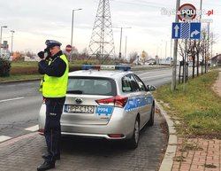 policjant ruchu drogowego przy radiowozie mierzy prędkość laserowym miernikiem