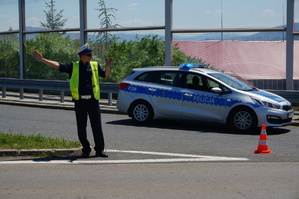 dzień, słonecznie, policjant ruchu drogowego obok oznakowanego radiowozu