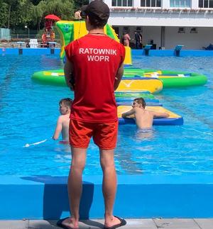 zdjęcie-ratownik w czerwonym stroju patrzy na kapiące się w basenie osoby