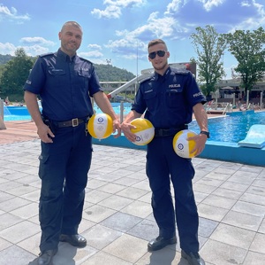 policjanci pozują do zdjęcia, trzymają piłki plażowe, w tle basen