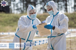 zdjęcie-jasno, policjanci ubrani w białe kombinezony czytają kartkę