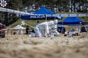 zdjęcie-teren, policjanci w kombinezonach zabezpieczają ślady w podłożu