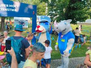 zdjęcie-słonecznie, rozbawione osoby, uśmiechnięte, stoisko z policyjnymi przedmiotami oraz radiowozem i quadem, maskotka policji pies Sznupek