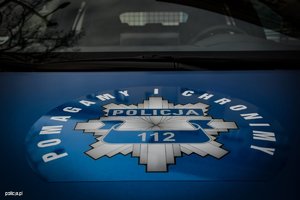 zdjęcie pokrywy silnika samochodu- naklejka z logo policji i napisem &quot;pomagamy i chronimy&quot;, oraz numerem 112