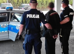zdjęcie-policjanci trzymają za ręce poszukiwanego, stoją przed radiowozem