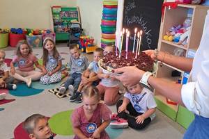 zdjęcie-tort ze świeczkami,przedszkolaki siedzą na podłodze, zabawki