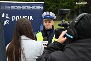 &quot;Policjant udzielający wywiadu telewizji TVS. Obok dziennikarka z mikrofonem oraz operator z kamerą.&quot;