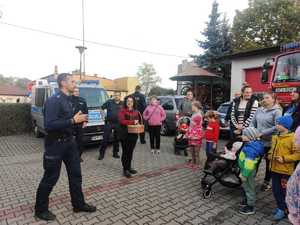 zdjęcie-policjant wręcza odblaski dzieciom, wszyscy są uśmiechnięci