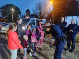 zdjęcie-policjant wręcza odblaski dzieciom, wszyscy są uśmiechnięci