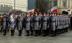 zdjęcie-dzień, policjanci w mundurach ustawieni w szyku, widoczne flagi Polski biało czerwone