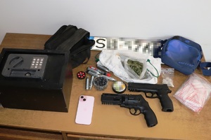 zdjęcie prezentuje zabezpieczone rzeczy-na stole leżą dwa pistolety, narkotyki, sejf, tablicarejestracyjna