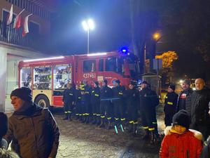 zdjęcie- strażacy stoją z odblaskami obok wozu straży pożarnej