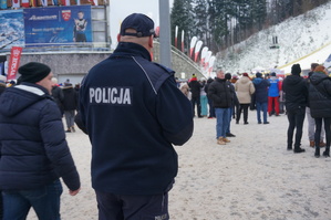 zdjęcie-zima, śnieg, droga, policjant kieruje ruchem, w tle skocznia narciarska