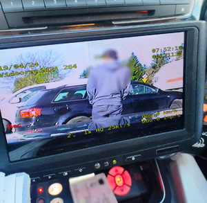 widok ekranu rejestratora-widoczny mężczyzna w bluzie z kapturem, odwrócony plecami, przed ni samochód