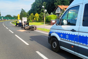 zdjęcie-miejsce wypadku, dzień, słonecznie, droga, wywrócony na jezdni motocykl, przed nim pojazd policji