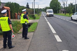zdjęcie-dzień ,policjanci stoją na poboczu drogi z miernikiem prędkości, mierzą prędkość nadjeżdżającego pojazdu