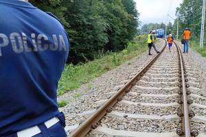 zdjęcie- dzień, torowisko, policjant, w tle pociąg, pochmurno