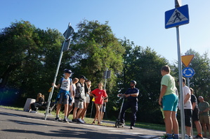 zdjęcie- dzień, słonecznie, dzieci i policjanci ćwiczą wspólnie jazdę na hulajnodze w miasteczku ruchu