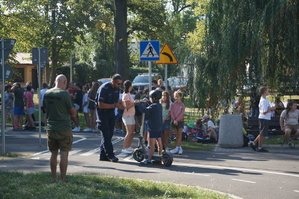 zdjęcie- dzień, słonecznie, dzieci i policjanci ćwiczą wspólnie jazdę na hulajnodze w miasteczku ruchu