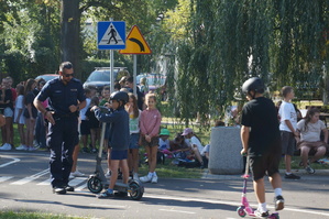 zdjęcie- dzień, słonecznie, dzieci i policjanci ćwiczą wspólnie jazdę na hulajnodze w miasteczku ruchu