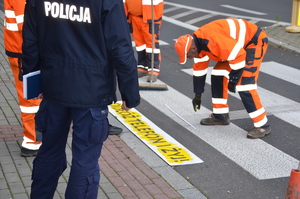 policjant pomaga przy malowaniu napisu odłóż telefon i żyj na przejściu dla pieszych