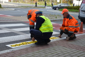 policjant pomaga przy malowaniu napisu odłóż telefon i żyj na przejściu dla pieszych