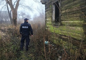 zdjęcie- policjant stoi obok starego budynku, mgła, dzień