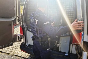 zdjęcie- jasno, słonecznie, policjant zamyka drzwi radiowozu