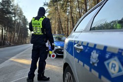 policjant z tarczą do zatrzymywania pojazdów stoi przy radiowozie na drodze, dzień, obserwuje ruch
