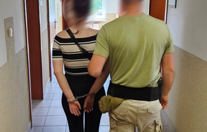 korytarz, policjant pilnuje kobietę, która ma kajdanki na rękach trzymanych z tyłu