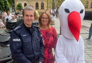 dzielnicowy, obok kobieta i maskotka bociana, słonecznie, płyta rynku