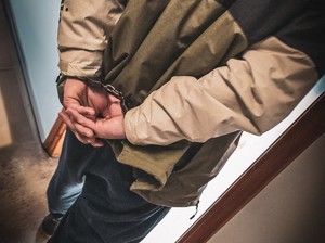 mężczyzna z kajdankami na rękach z tyłu wchodzi do pomieszczenia