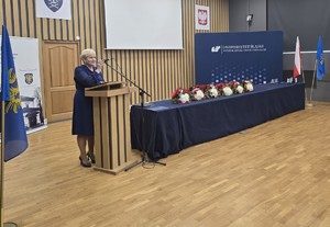 osoba stoi za mównicą i przemawia do zgromadzonych gości