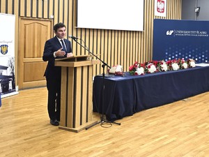 osoba stoi za mównicą i przemawia do zgromadzonych gości