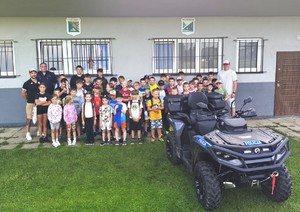 policjant pozuje  z dziećmi do zdjęcia, pochmurnie, przed nimi stoi na trawie quad policji