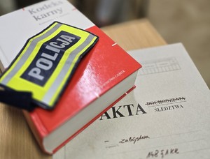 akta sprawy i kodeks na stole oraz opaska z napisem policja