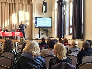 zdjęcia z sali, prelegenci przemawiają, osoby zgromadzone siedzą na krzesłach i słuchają ,