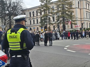 osoby maszerują, dużo flag Polski, pochmurno, widać poczet sztandarowy