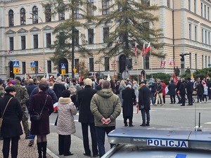 osoby maszerują, dużo flag Polski, pochmurno, widać poczet sztandarowy